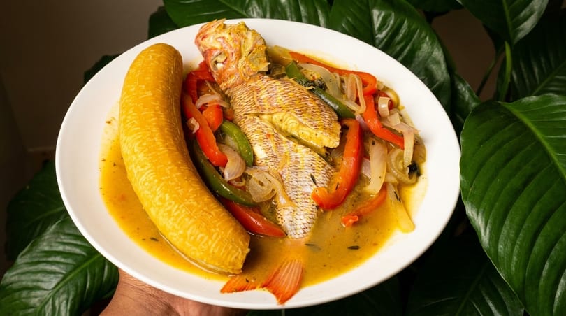 Whole steamed fish with bell peppers, onions, and a plantain in a rich sauce.