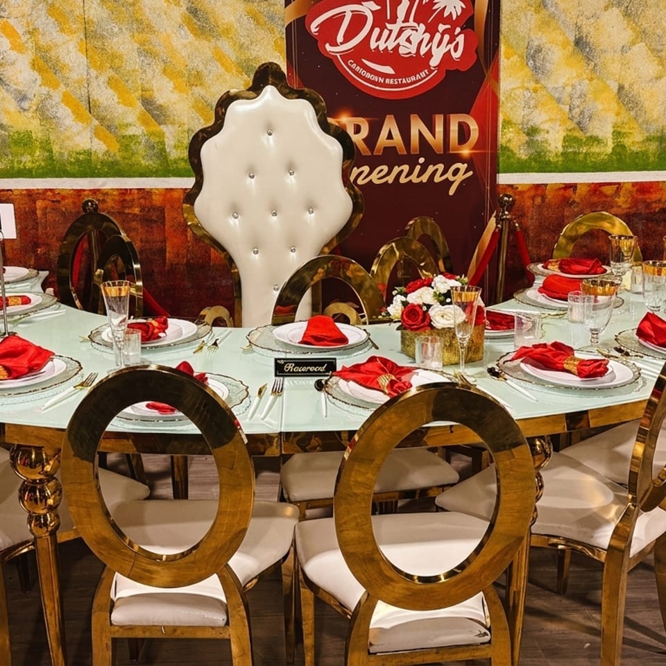 An elegantly set table with gold chairs, red napkins, and floral centerpieces, ready for a grand opening.