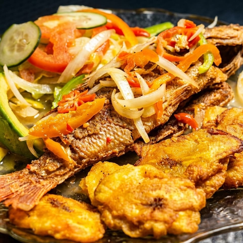 Fried whole fish topped with onions and peppers, served with avocado slices, salad, and fried plantains.