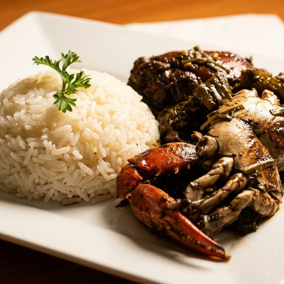 A white plate with a mound of white rice and a serving of dark, saucy crab and chicken.