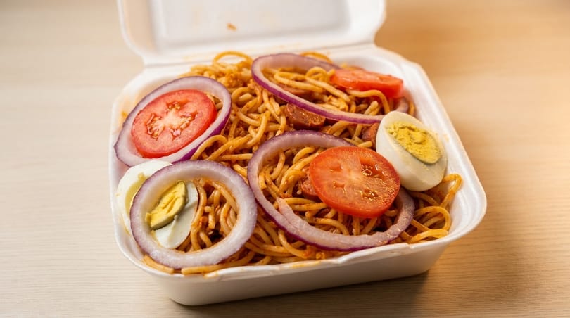 Spaghetti with sliced tomatoes, red onions, and hard-boiled eggs in a white takeout container.